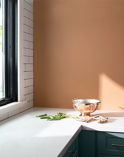 Cocina con paredes pintadas de durazno, pared de acento con azulejos de estilo metro, encimeras azules con sobres blancos y un bol de latón.