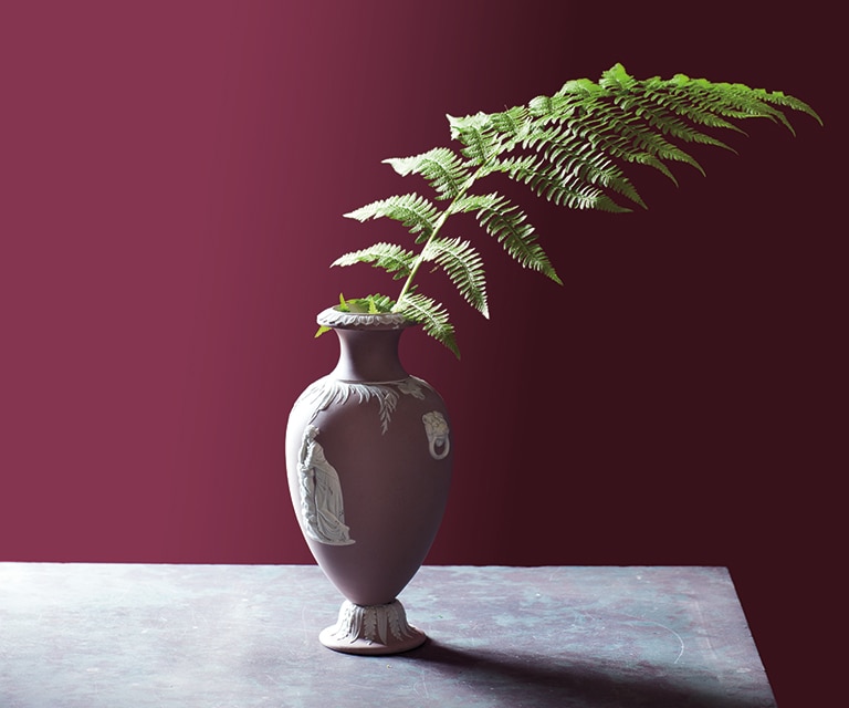 A vase sitting on a table in front of a deep red wall.