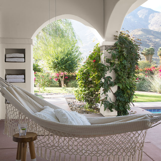 A white hammock in an exterior space with columns, a pool, and view of desert mountains and foliage.