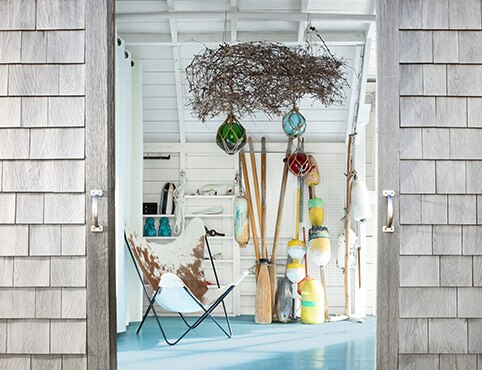 The white-painted interior of a coastal boathouse is seen through stained sliding barn doors.