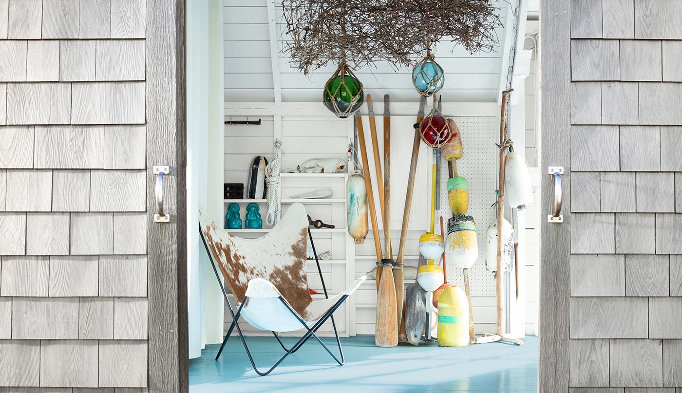 The white-painted interior of a coastal boathouse is seen through stained sliding barn doors.