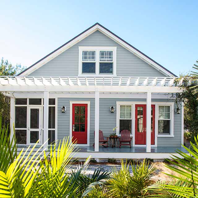 Maison peinte en gris avec porte d’entrée rouge et moulures blanches.
