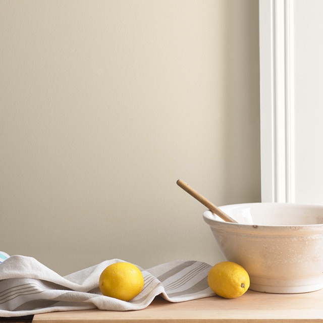 Un bol à mélanger qui contraste avec un mur Mousseline OC-12 et des moulures blanches sur un comptoir où reposent des citrons et un linge à vaisselle.
