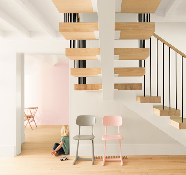 Escalera de madera flotante en un vestíbulo abierto con paredes blancas y una pared de acento rosa. Escalera de madera flotante en un vestíbulo abierto con paredes blancas y una pared de acento rosa.