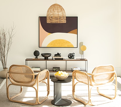 White walls with a long wall table, two rattan chairs and a black side table. 