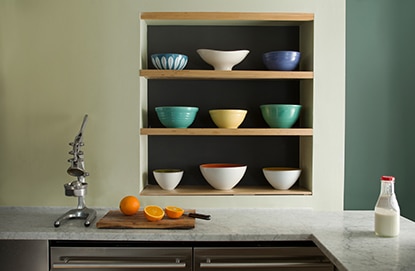 Monochromatic kitchen walls with shades of dark and light green including three inset shelves holding 9 bowls.