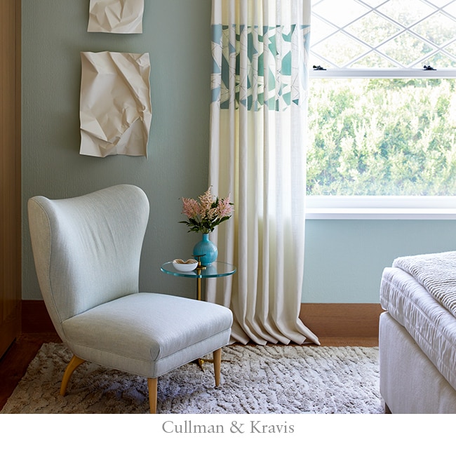 Warm blue-green walls with floor to ceiling curtains and an off-white accent chair