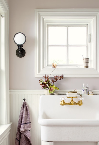 Un lavabo blanc surdimensionné devant un mur lavande pâle orné de lambris blancs.
