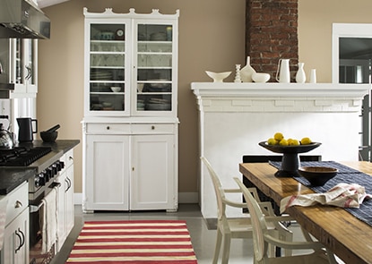 Tan kitchen walls with a white armoire, white fireplace, and a red and white striped floor runner.