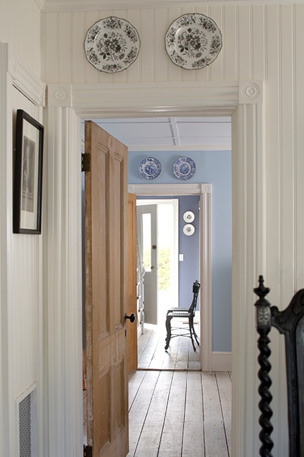 White paneled walls leading into a misty blue room with light brown doors.