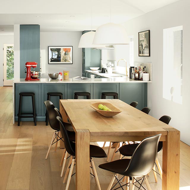 Un espace de vie à aire ouverte arborant un foyer de pierre, des fauteuils en cuir, un îlot de cuisine gris-bleu et une table à manger en bois. 