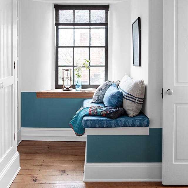 White-painted hallway with built-in bench, blue wainscoting, black accents, blue cushions and pillows.