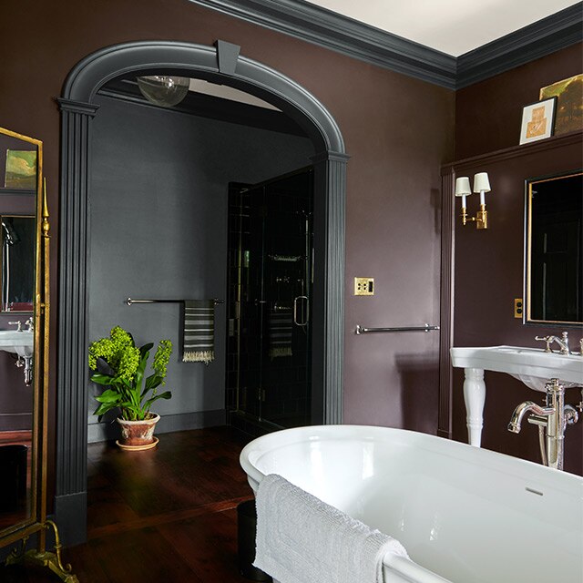 Une grande salle de bains aux murs brun foncé arborant des moulures noires, une baignoire, des accents dorés et une entrée gris foncé.