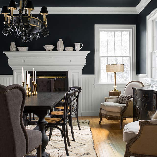 A black dining room with white trim and wainscoting, ornate chandelier, black table and chairs, and additional seating.
