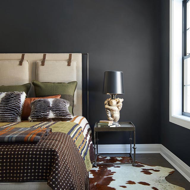 Une chambre avec des murs peints en noir, des moulures de fenêtre blanches et un tapis à imprimé animalier.