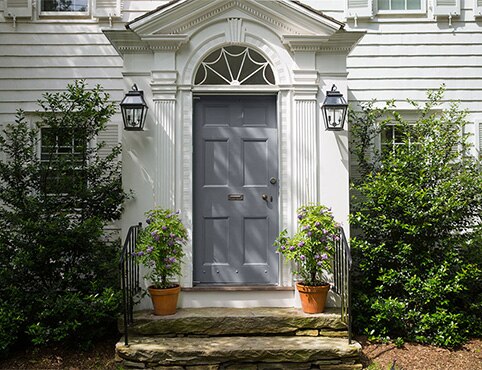 A colonial style front entrance with gray-painted front door and stone steps.