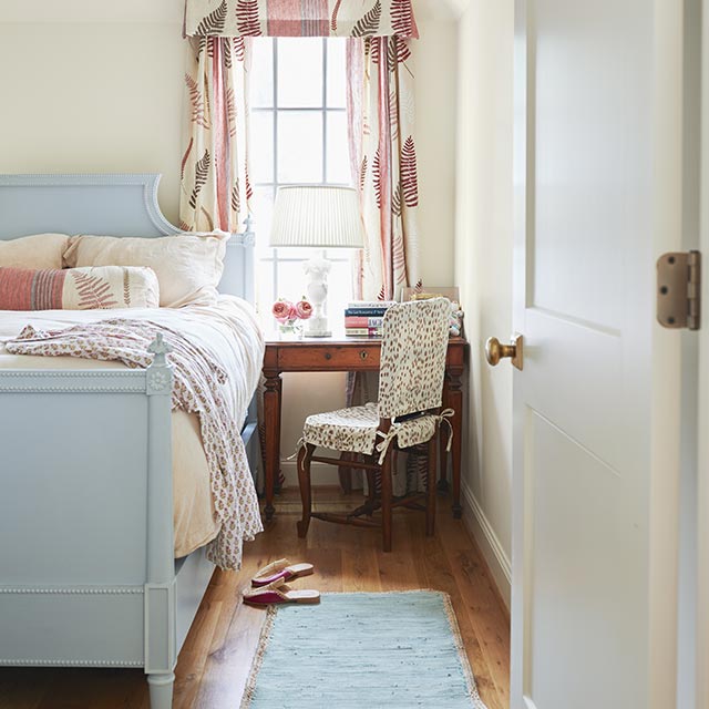 A French country bedroom with white-painted walls and door, a blue-painted ceiling and bedframe, patterned curtains, and wood floor.