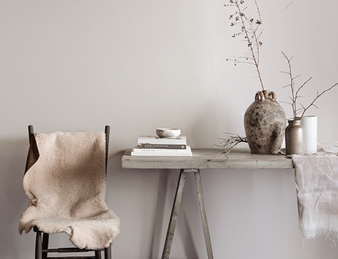 Gray dining area featuring a rustic table with books, vases, and branches, and chair topped with white fur blanket.