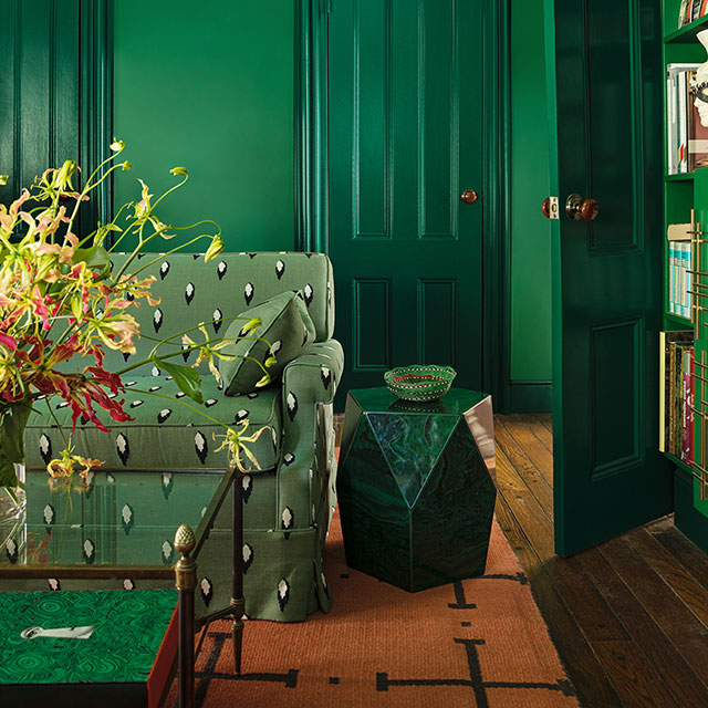 A green-painted living room with a green-printed couch, stone end table, glass coffee table and bookshelves matching the walls.