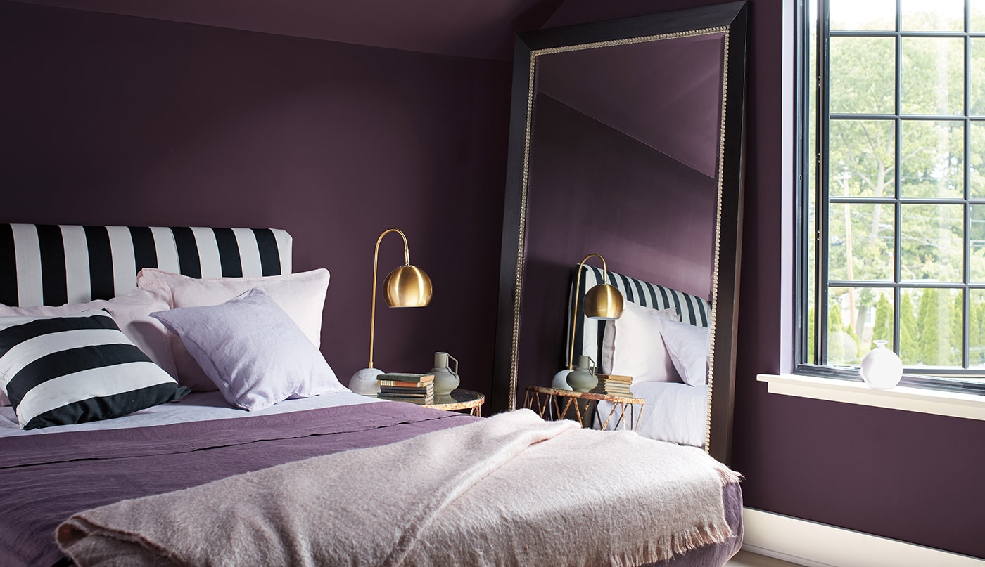 A dark purple-painted bedroom with white trim, a black and white striped headboard and pillow, and purple and white blankets.