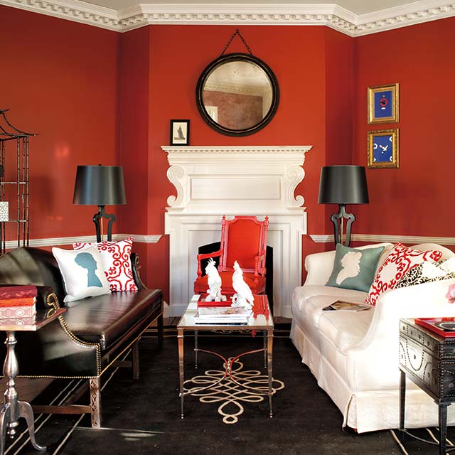 Salon rouge de style classique avec manteau de cheminée, plafond et moulures blancs, sofa blanc et noir, et plancher décoratif foncé.
