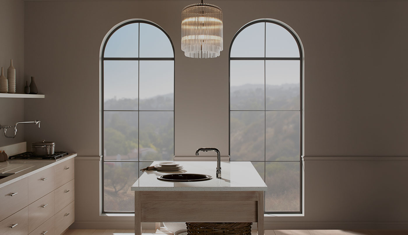 A kitchen with beige walls, two large arch windows, and an island with a sink.