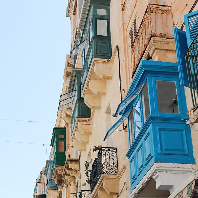 Un immeuble beige avec des balcons fermés aux nuances de bleu et de vert.