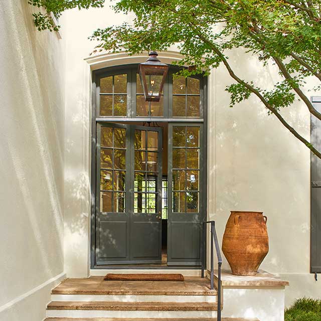 Une entrée extérieure présentant une grande porte munie de nombreuses fenêtres, des escaliers, des pots en terre cuite et un arbre.
