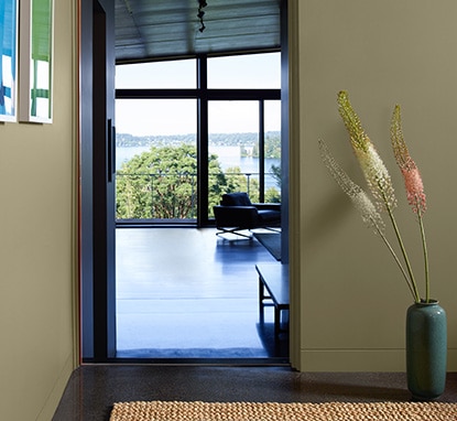A muted green room with an opened door leading into a room with large floor to ceiling windows.
