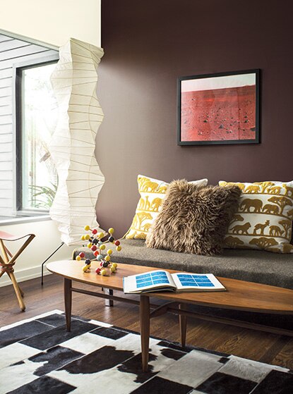 A couch with three throw pillows and a wood coffee table in a midcentury modern living room with one white wall and one brown wall.