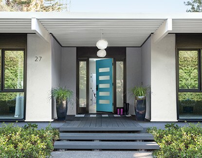 A modern light grey home with black window trim and a vibrant blue front door.