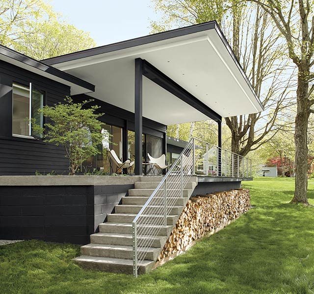 A modern style home with black painted exterior siding, and stairs leading to a porch with a white ceiling and black posts.
