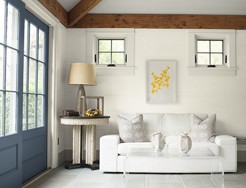 Gray-painted doors provide a warm welcome into this white-painted seating area with a white couch and modern furniture.