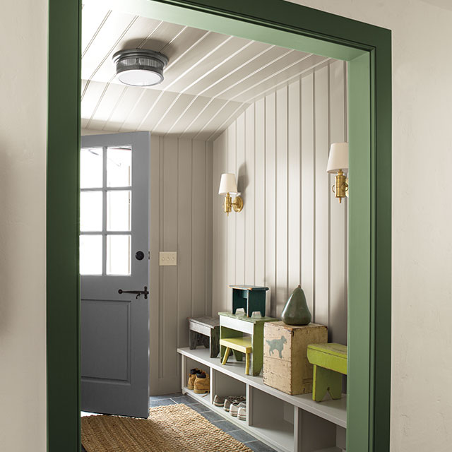 Entryway with white shiplap walls and green trim, featuring wall lighting and cubbyholes with boots.