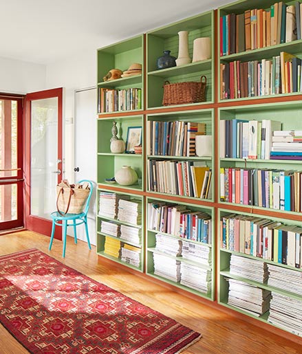 An entryway with red-trimmed door, print red rug, and green-painted bookcase.