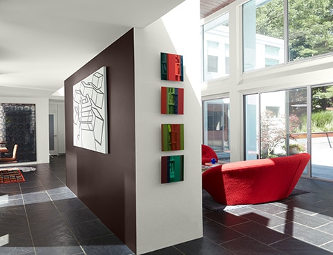 Une pièce de style rétro arborant des murs et un plafond peints en blanc, un mur d’accent brun, de grandes fenêtres et un fauteuil rouge.
