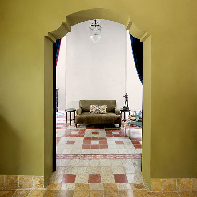 A yellow-green painted wall and archway outside of a white living room with colourful tile floors.