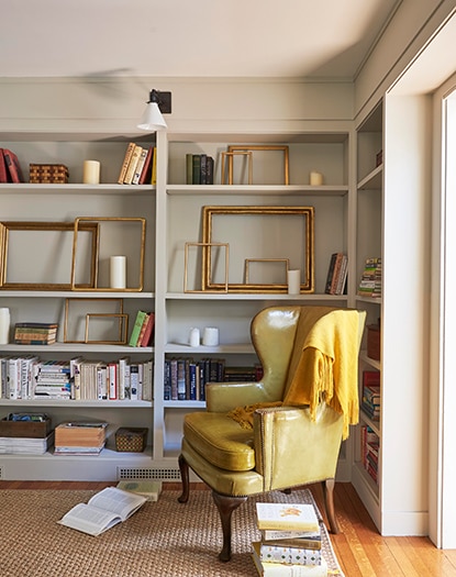 Taupe-painted library with built-in shelves, books, emtpy frames, and a large armchair. 