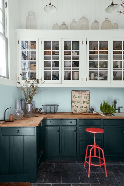 An eclectic kitchen with dark blue counters, white cabinets, a red stool, and various kitchen utensils.