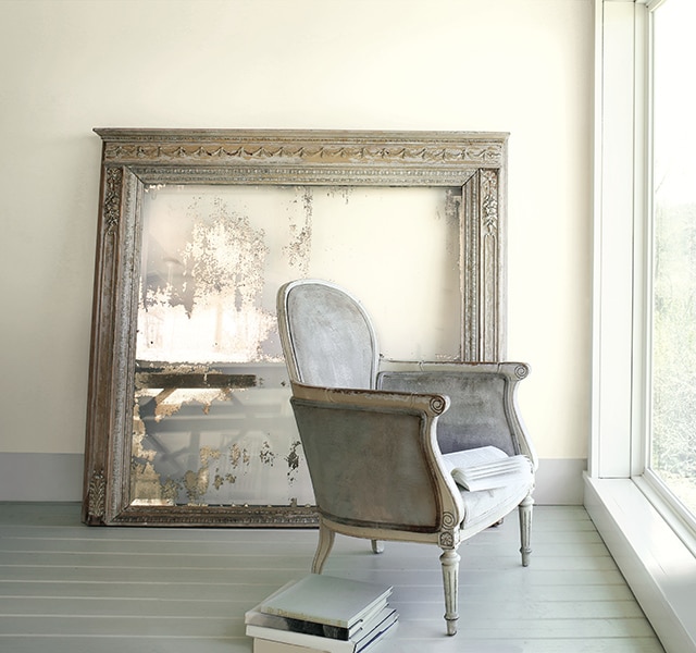 A gray armchair in front of a large window in a beige-painted room featuring a large frame. 