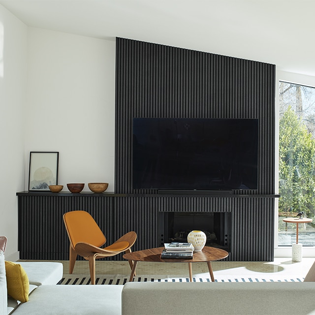 Salon moderne inspiré des années 1950 avec murs et plafond en voûte d’un blanc lumineux, mur d’accent en panneaux noirs, cheminée et téléviseur grand écran.