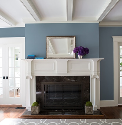 A white fireplace and mantel in a blue living room with windowed double doors.