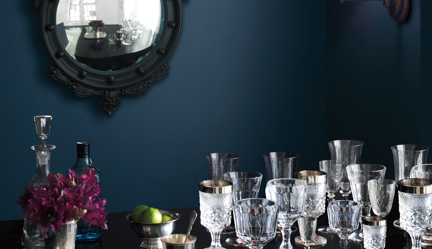 A dark blue-painted dining room wall frames ornate glasses on a table.