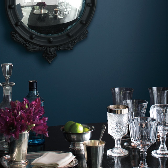 A dark blue-painted dining room wall frames ornate glasses on a table.