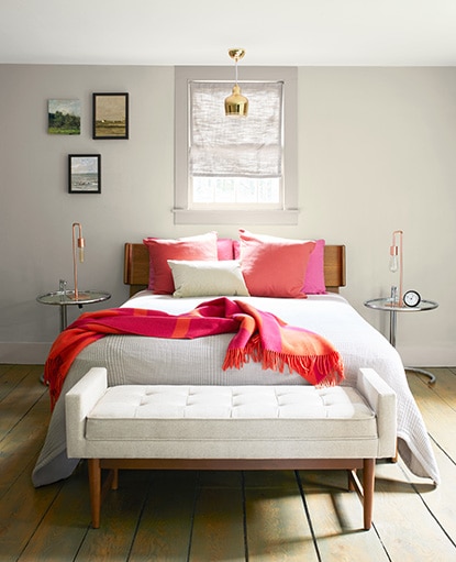 Chambre à coucher neutre aux murs Crème Naturelle OC-14 avec des coussins décoratifs et une couverture rouge vif.