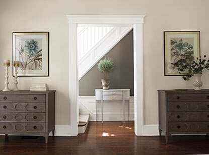 Un corridor gris avec un escalier et un lambris d’appui blancs se caractérise par une exquise console d’applique et de brillants planchers de bois francs.