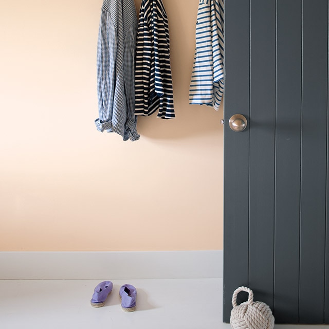A peach-painted wall with white trim and gray doors, featuring a set of white coat hooks with various shirts.