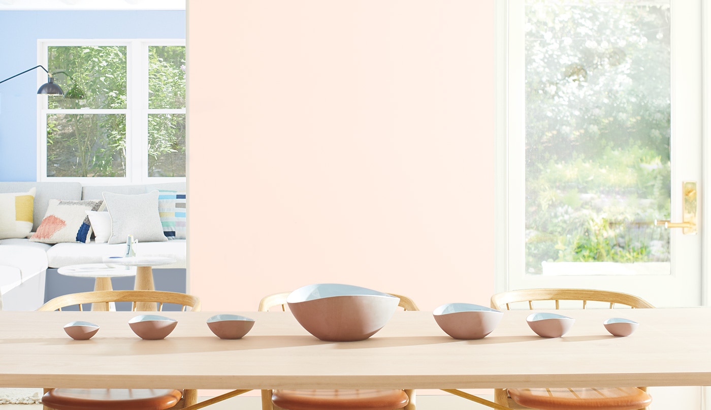 Une salle à manger aux murs peints en rose clair décorée d’une longue table en bois, de chaises assorties et de bancs.