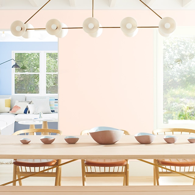 Light pink-painted dining room walls with a long wooden table, matching chairs and bench seating.