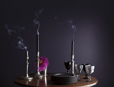 Une table en bois sur laquelle sont posés des verres, des assiettes et des bougies devant un mur pourpre foncé.